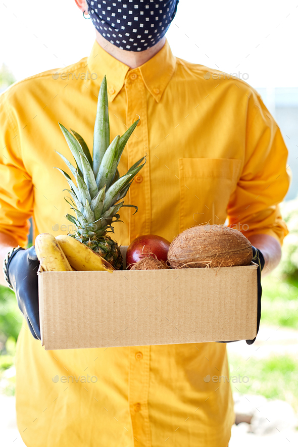 Courier man delivery box with exotic fruits food, contactless delivery